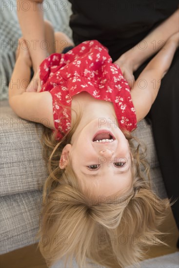 Caucasian mother tickling daughter on sofa