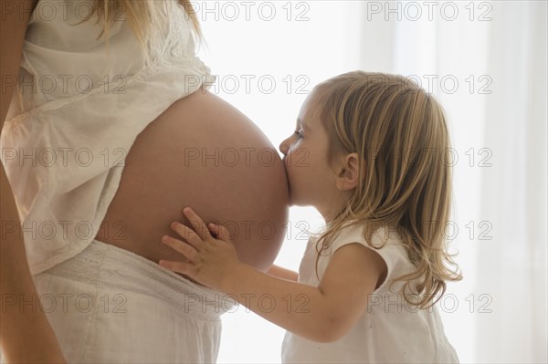 Caucasian girl kissing belly of pregnant mother