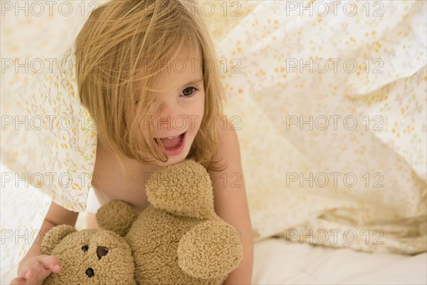 Caucasian girl playing with teddy bear under blankets