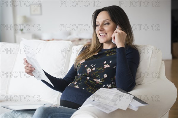 Pregnant Caucasian woman paying bills over phone