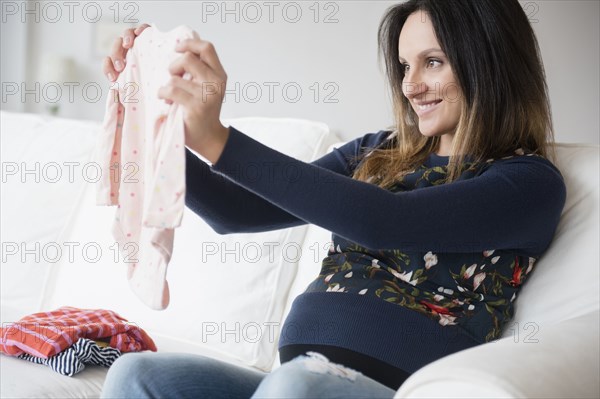 Pregnant Caucasian woman admiring baby clothing