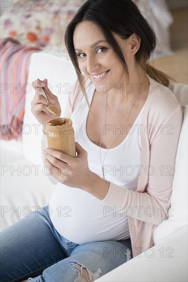 Pregnant Caucasian woman eating peanut butter from jar