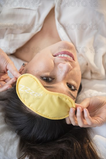 Smiling woman wearing eye mask on bed