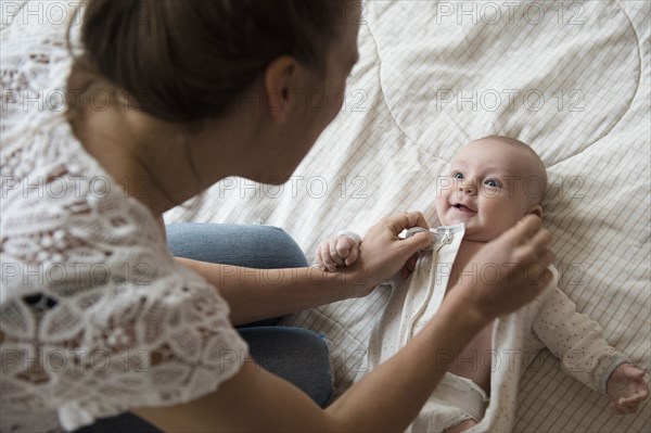 Caucasian mother dressing baby on bed