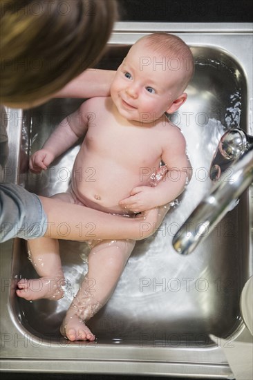 Caucasian mother bathing baby in sink