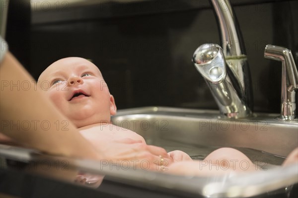 Caucasian mother bathing baby in sink