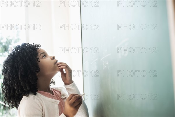 African American student writing on chalkboard in classroom