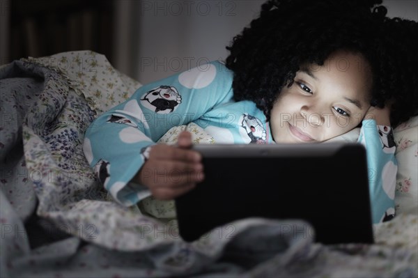 African American girl using digital tablet in bed