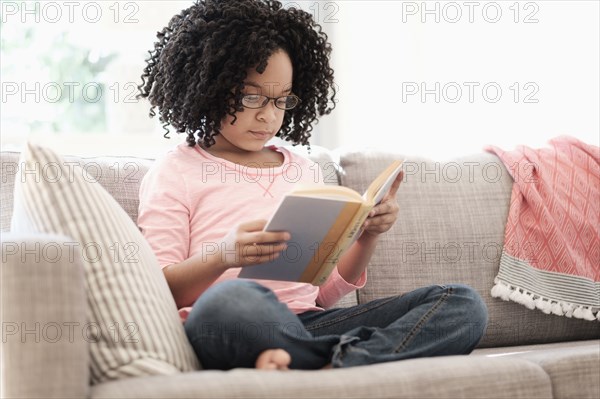 African American girl reading book on sofa