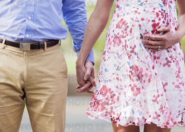 Pregnant Caucasian couple holding hands outdoors