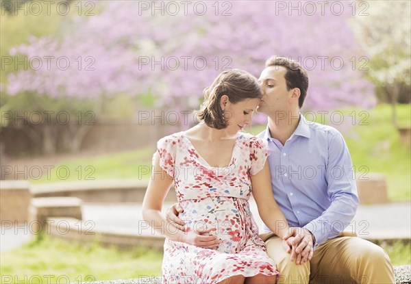 Pregnant Caucasian couple kissing outdoors