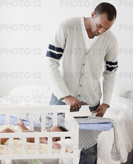 African man ironing shirt near baby in crib