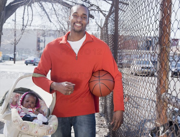 African man carrying baby in carrier and holding basketball