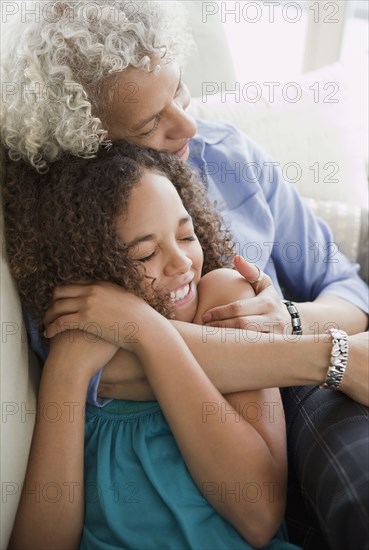 Grandmother and granddaughter hugging on sofa