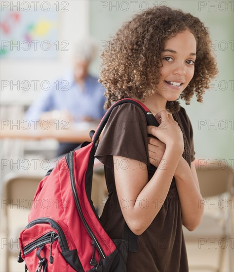 Mixed race girl holding backpack in classroom