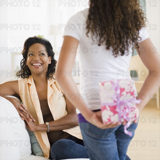 Daughter holding birthday gift behind back for mother