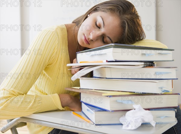 Tired Indian student laying on stack of textbooks
