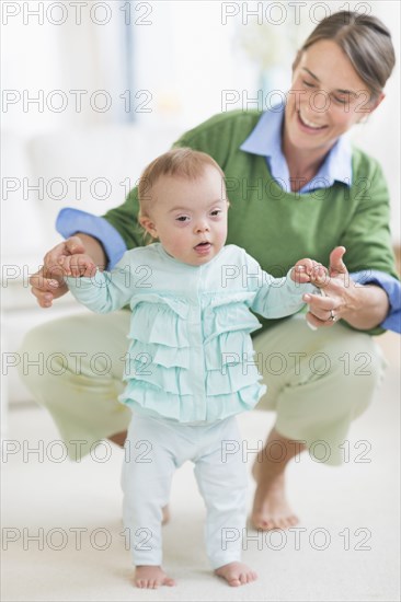 Caucasian mother helping baby with Down Syndrome walk