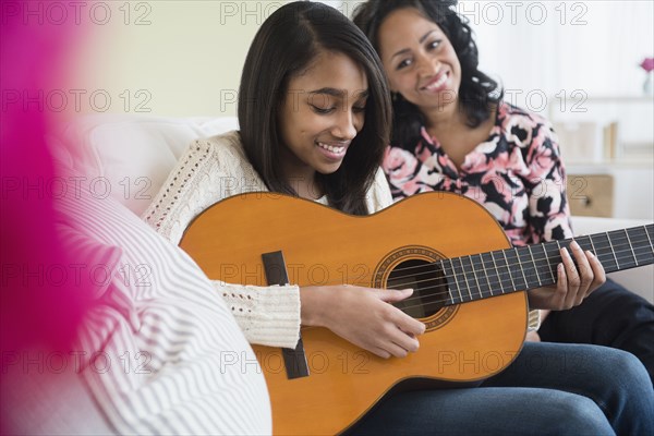 Mother watching daughter play guitar on sofa