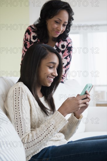 Mother watching daughter use cell phone on sofa