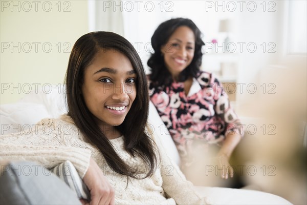 Smiling mother and daughter sitting on sofa