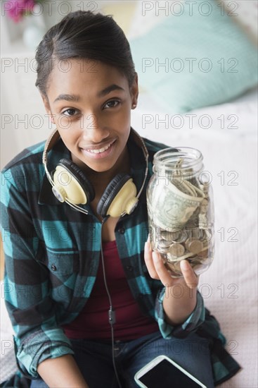 Mixed Race girl holding jar containing cash and coins