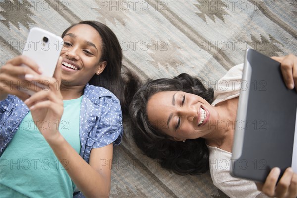 Mother and daughter laying on carpet using cell phone and digital tablet