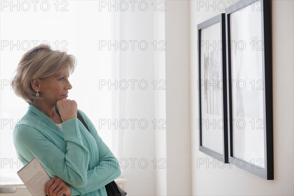 Older Caucasian woman examining artwork in gallery