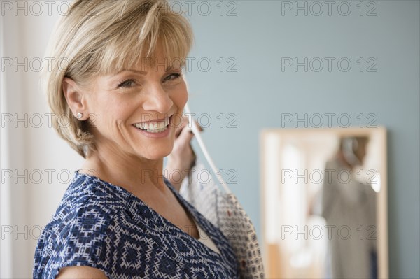 Smiling older Caucasian woman holding clothing near mirror