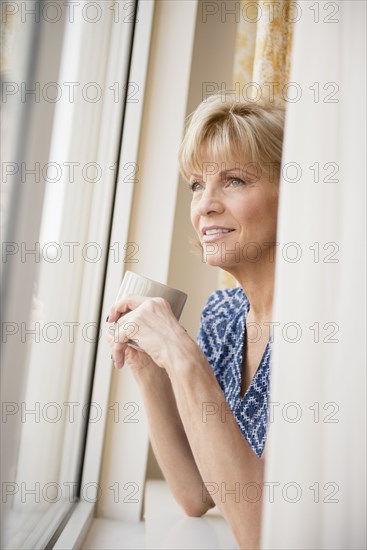 Older Caucasian woman drinking coffee at window
