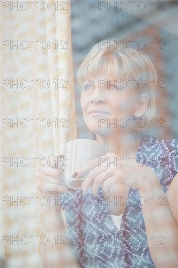 Older Caucasian woman drinking coffee at window