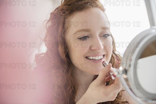 Caucasian woman applying lipstick in mirror