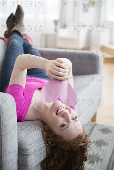 Caucasian woman laying on sofa holding valentine heart