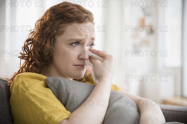 Crying Caucasian woman clutching pillow wiping tears