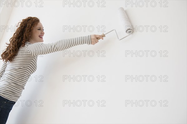 Caucasian woman painting wall white with paint roller