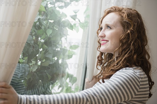 Caucasian woman opening curtains at window