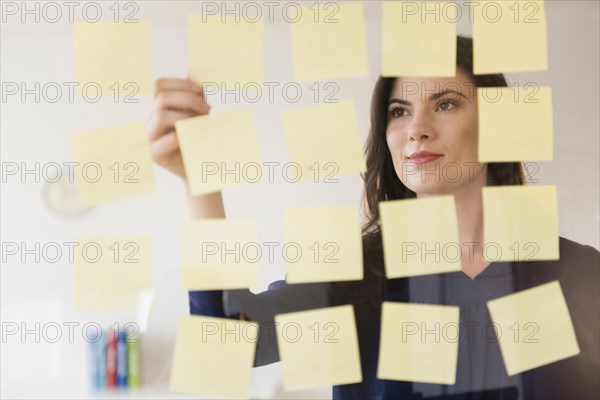 Caucasian businesswoman arranging adhesive notes on glass wall