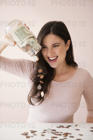 Caucasian woman pouring jar of money onto table