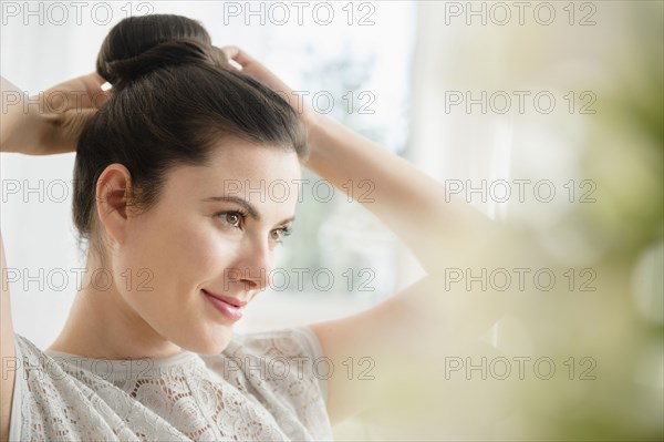 Caucasian woman tying hair in bun