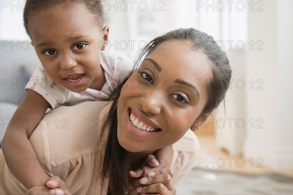 Black mother carrying baby daughter piggyback