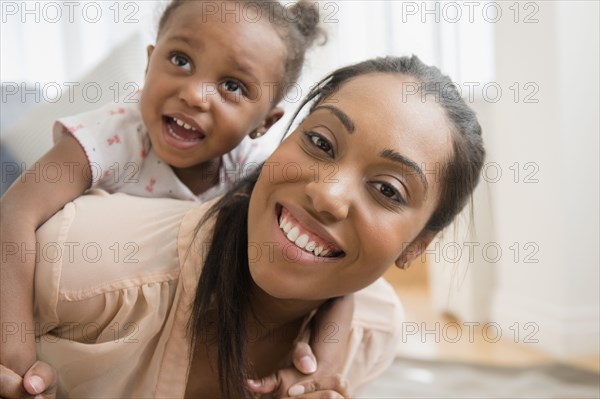 Black mother carrying baby daughter piggyback