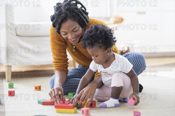 Black mother and baby daughter playing with blocks on carpet