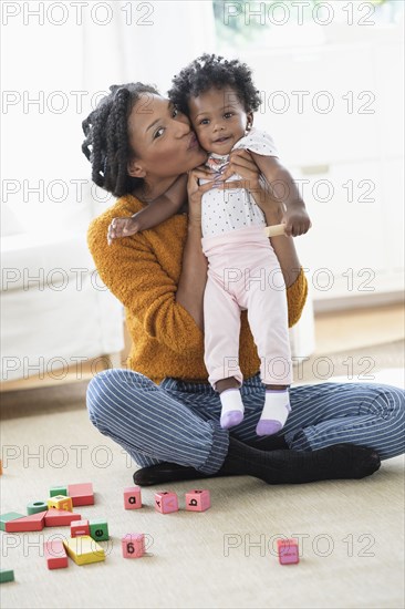 Smiling Black mother kissing baby daughter