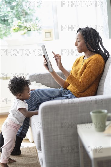 Black woman using digital tablet on sofa near baby daughter