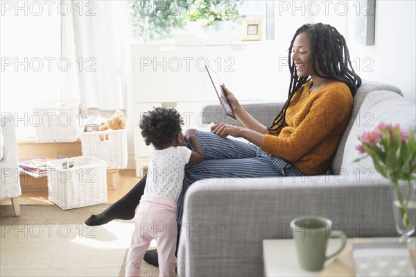 Black woman using digital tablet on sofa near baby daughter