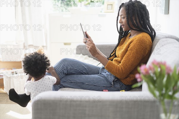 Black woman using digital tablet on sofa near baby daughter