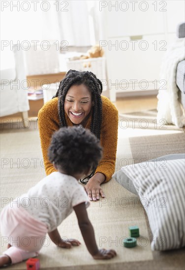 Black woman playing with baby daughter on carpet