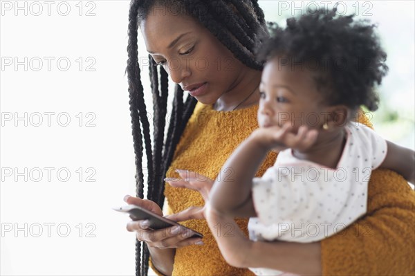 Black woman holding baby daughter using cell phone