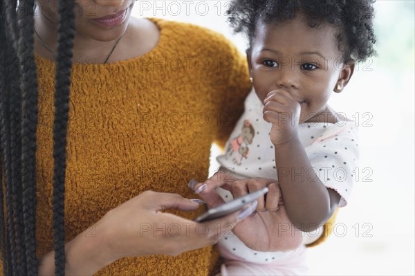 Black woman holding baby daughter using cell phone