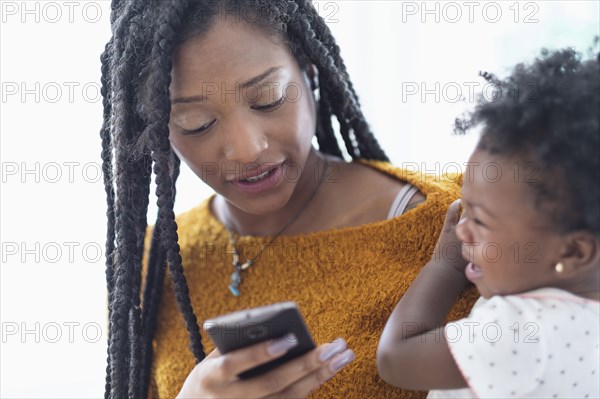 Black woman holding baby daughter using cell phone